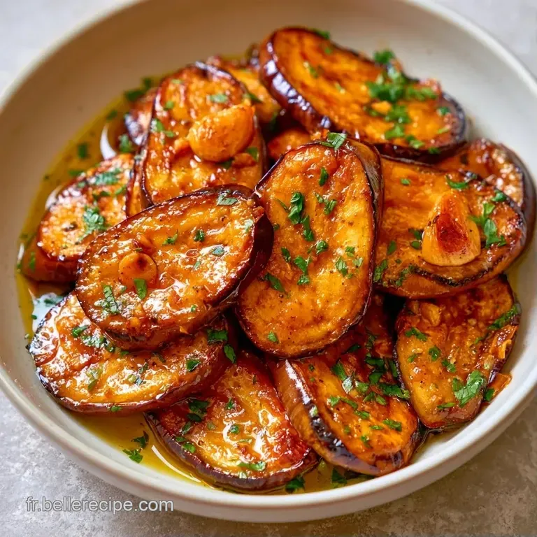 Tranches d'aubergines fondantes dispos&eacute;es en &eacute;ventail sur une assiette blanche, parsem&eacute;es d'herbes vertes et d'huile.